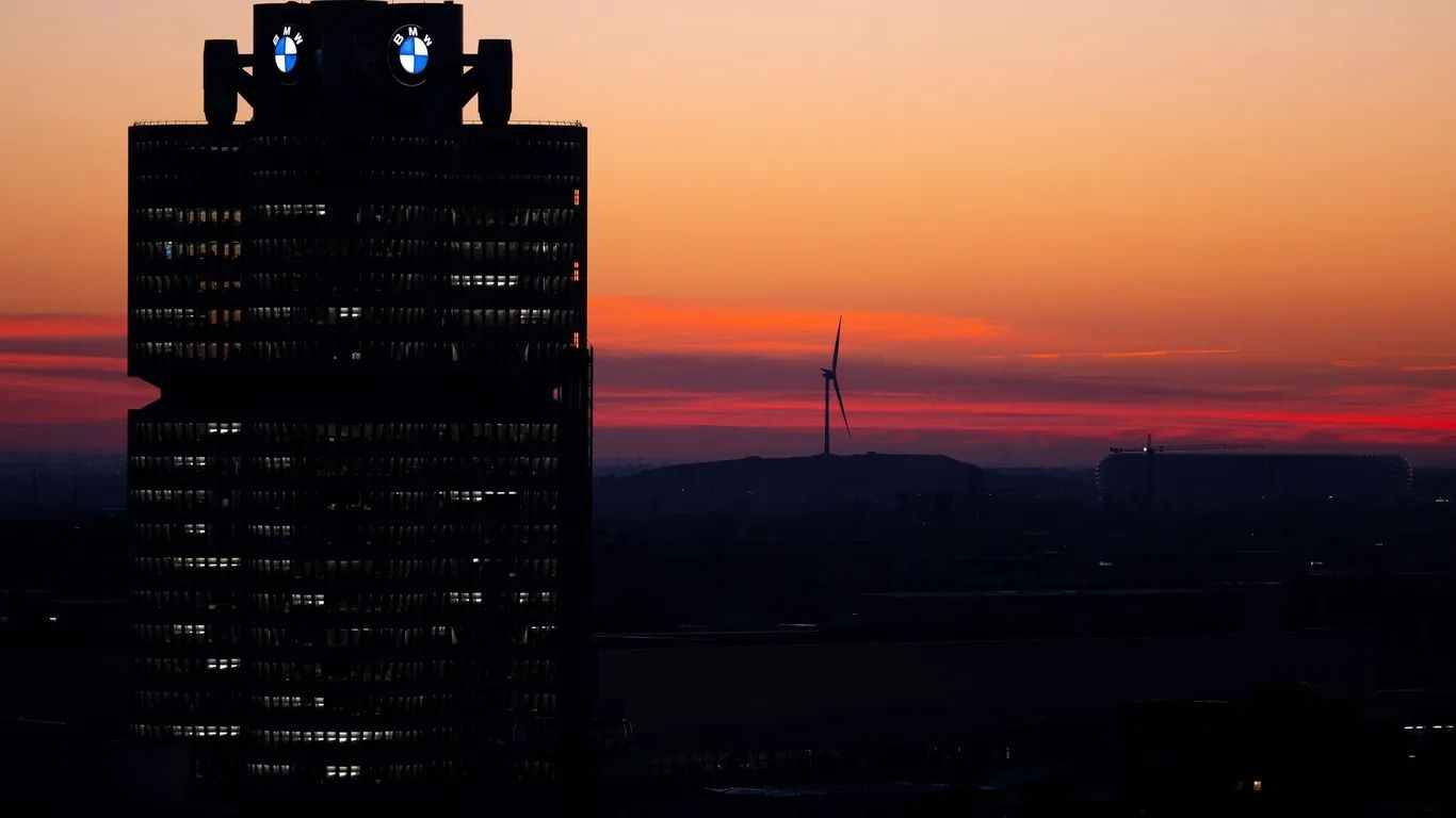Die Silhouette des BMW-Hochhauses in München vor dem Abendhimmel, am Horizont ein Windrad