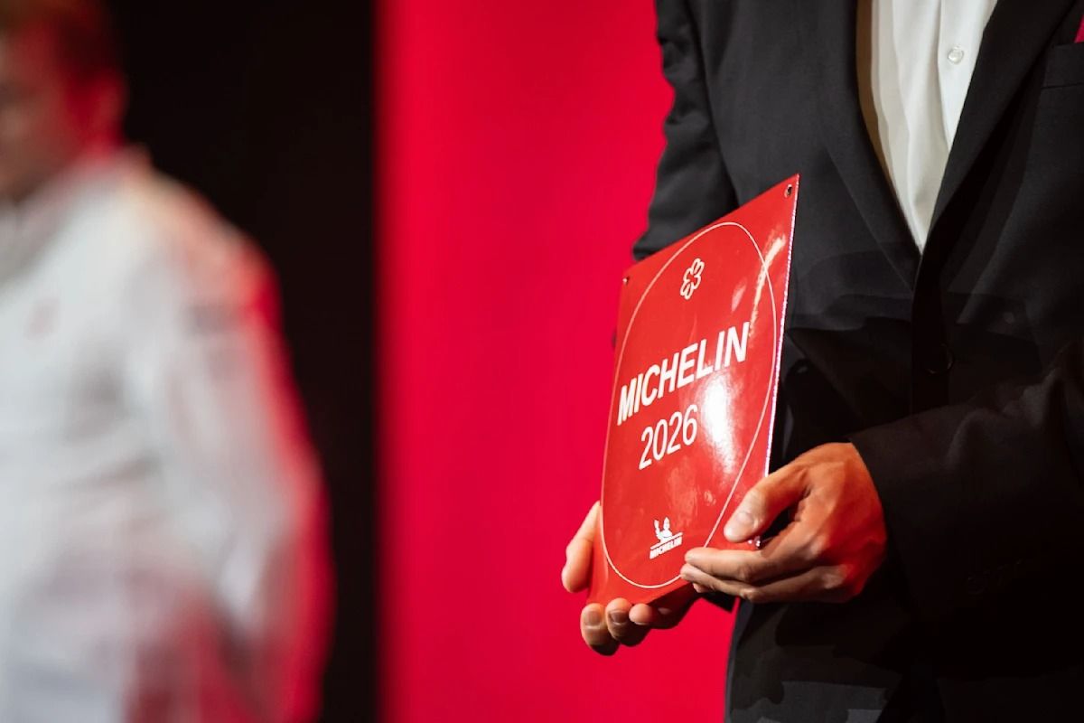 Ein Mann im Anzug hält die rote Michelin-Plakette des Jahrgangs 2026