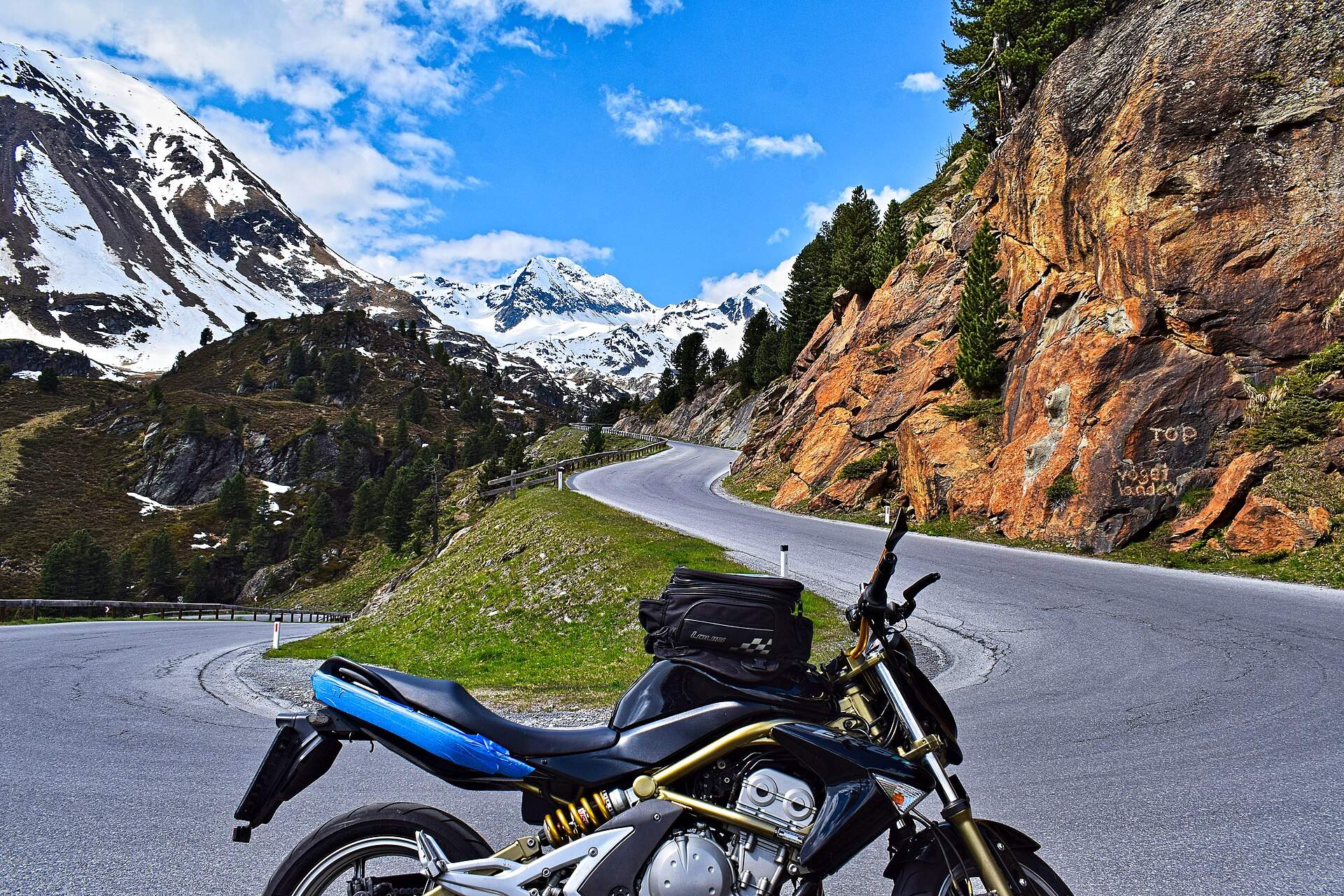 Motorrad in der Kehre einer Alpenpassstraße vor Schneegipfeln